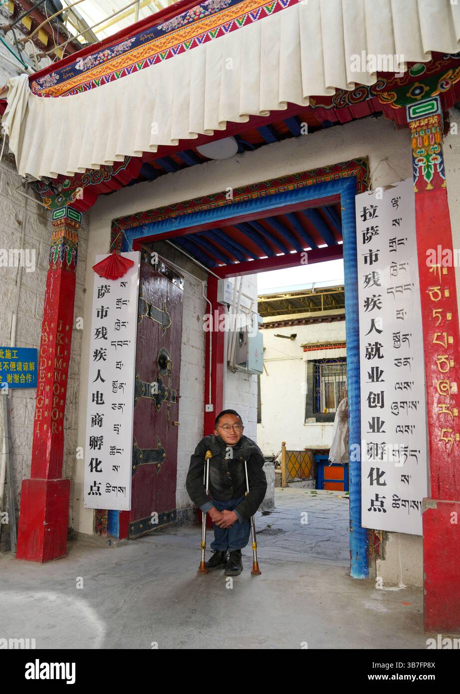 (250506) -- LHASA, 6. Mai 2025 (Xinhua) -- Lhapa Dondrup ist am Eingang des Unternehmens in Lhasa, südwestchinesischer Autonomen Region Xizang, 5. Mai 2025 abgebildet. Lhapa Dondrup, ein 24-jähriger Mann, der in Lhasa geboren wurde, leidet seit seiner Kindheit an Osteogenesis imperfecta (OI), allgemein bekannt als brüchige Knochenerkrankung. Als Erwachsener steht er unter einem Meter groß und verlässt sich auf Krücken und elektrischen Rollstuhl für Mobilität. Trotz dieser Herausforderungen träumt Lhapa davon, Fotograf zu werden. 2021 schloss er sich einem Kulturmedienunternehmen an, das von Menschen mit körperlicher Behinderung gegründet wurde Stockfoto