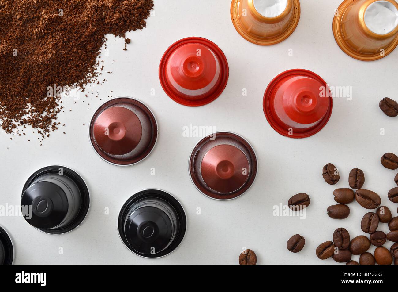 Reihe von mehrfarbigen Espresso-Kapseln mit verschiedenen Kaffeesorten auf einem weißen Tisch mit Kaffeebohnen und gemahlenem Kaffee. Draufsicht. Stockfoto