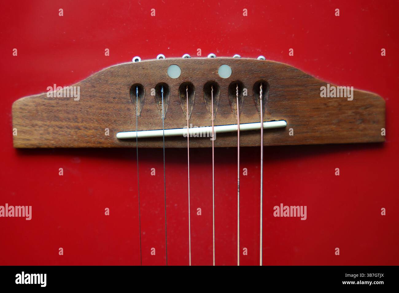 Nahaufnahme einer Gitarrenbrücke und Streicher auf einem leuchtend roten Hintergrund, die die Holz- und Metallic-Elemente des Instruments hervorheben Stockfoto Nahaufnahme einer Gitarrenbrücke und Streicher auf einem leuchtend roten Hintergrund, die die Holz- und Metallic-Elemente des Instruments hervorheben Stockfoto