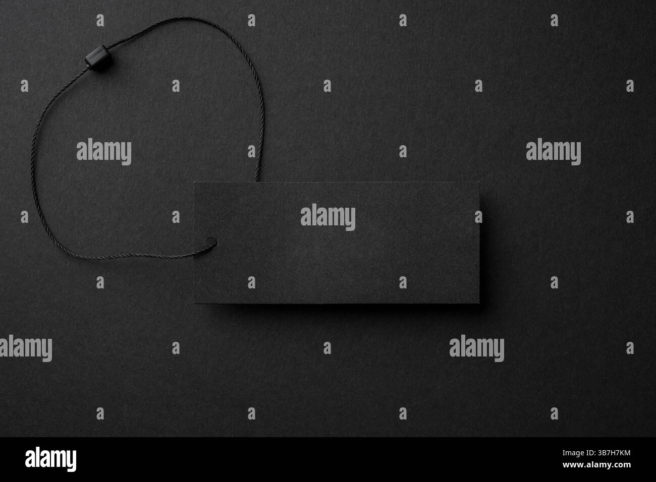 Leerer schwarzer Pappanhänger mit Schnur auf schwarzem Hintergrund Stockfoto