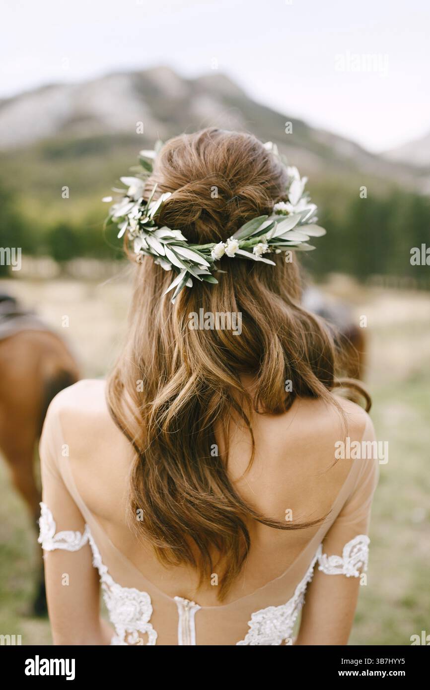 Die Braut steht mit ihrem Rücken in einem wunderschönen Spitzenkleid. Der Kopf der Braut ist mit einem Kranz aus grünen Olivenzweigen geschmückt. Stockfoto