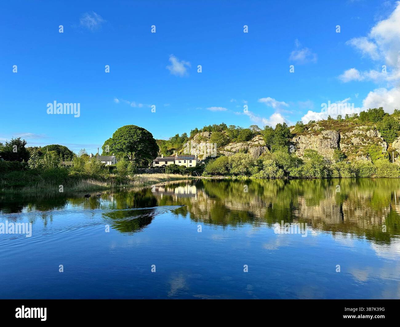 Steinhäuser mit Blick auf den Llyn Padarn See in Snowdonia, Wales, umgeben von Schiefer, Bäumen und fernen Bergen. - Smartphone-aufgenommenes Stockfoto