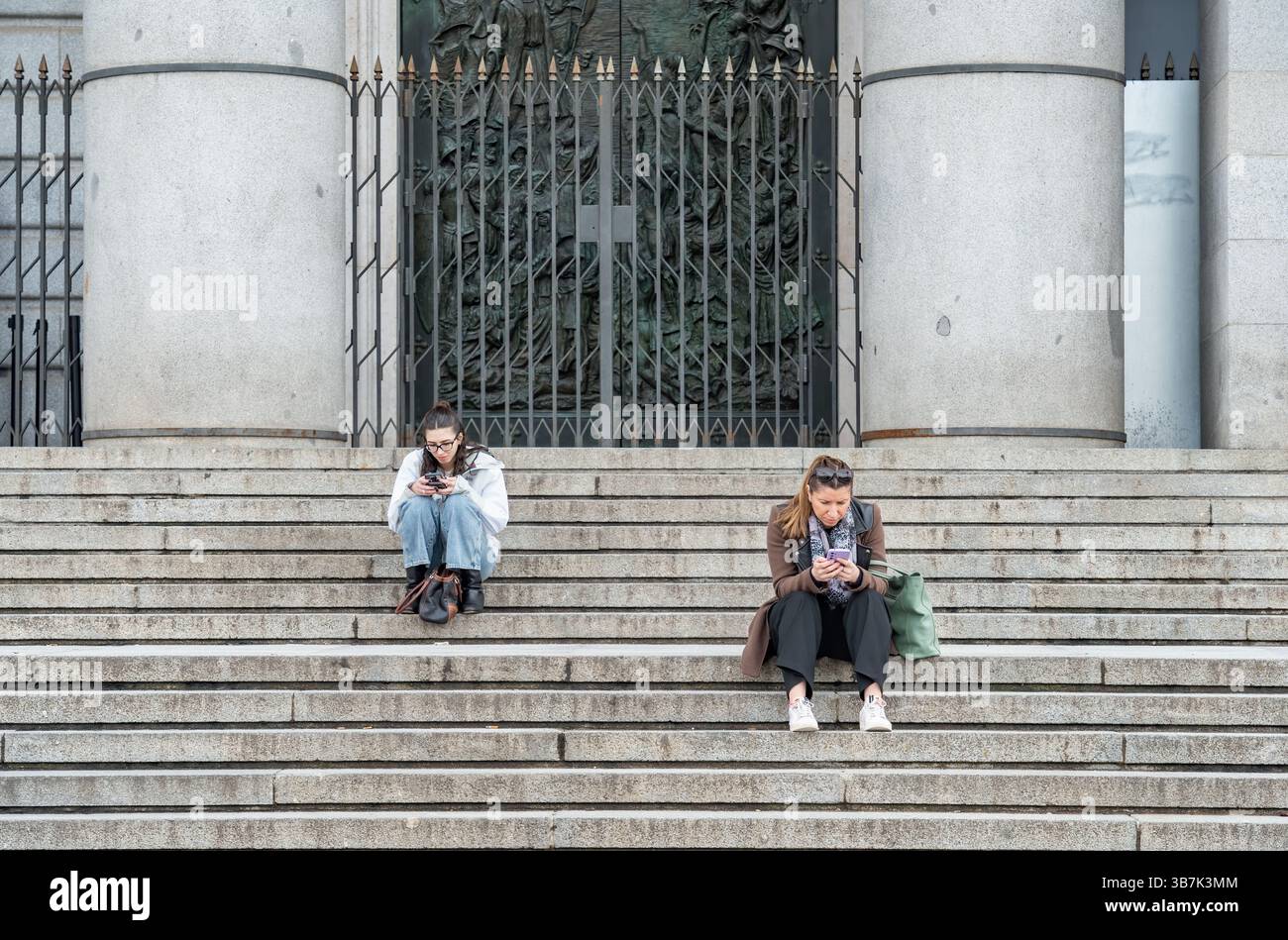 Madrid, Spanien - 03.10.2025: Zwei Mädchen oder Frauen ruhen sich auf der Treppe am Eingang der Kathedrale von Almudena aus Stockfoto