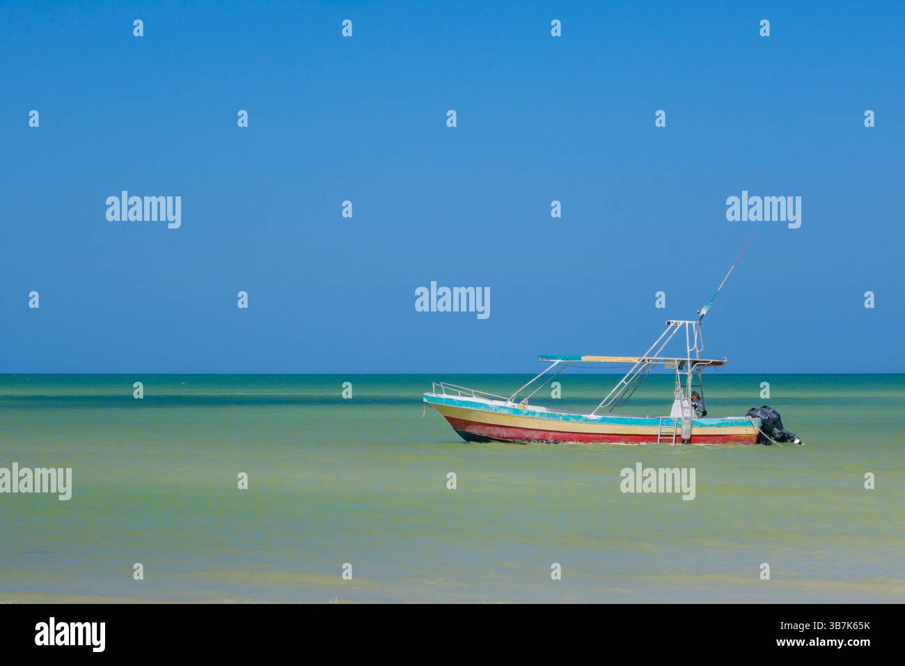 Ein einzelnes bemaltes Fischerboot ruht friedlich im flachen türkisfarbenen Wasser in Holbox Stockfoto