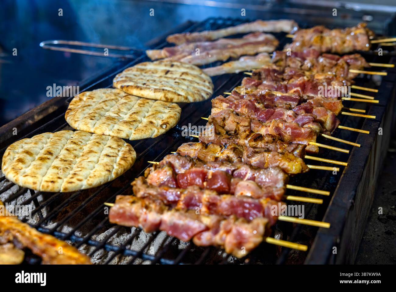 Gegrillte Fleischspieße, die über heißen Kohlen sickern, neben warmem, geröstetem Pita-Brot – ein unwiderstehlicher Geschmack mediterraner Street Food Stockfoto