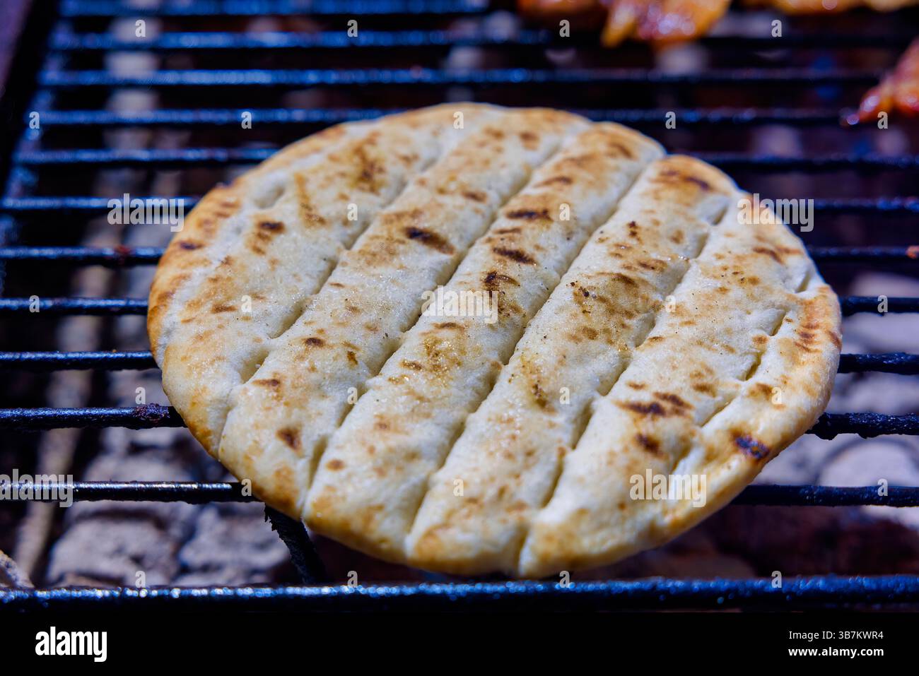 Ein Stück Fladenbrot wird gegrillt, das knackige Grillspuren aufweist. Die goldbraune Oberfläche hebt die Textur hervor und fängt einen köstlichen Kochmoment ein Stockfoto
