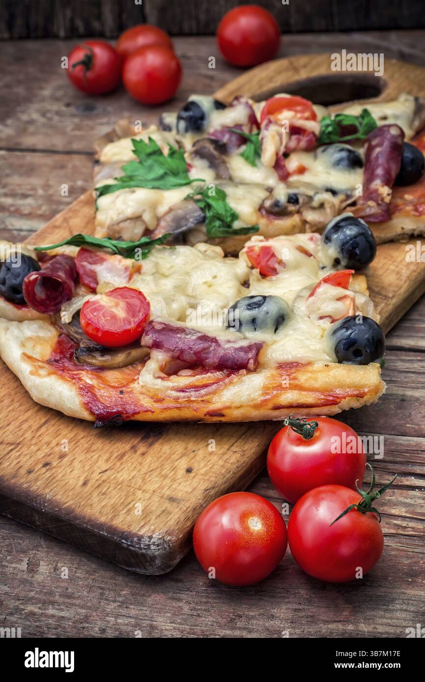 Fleischpizza mit Salami, Käse, Pilzen, Kirschtomaten und Oliven. Das Bild ist getönt Stockfoto