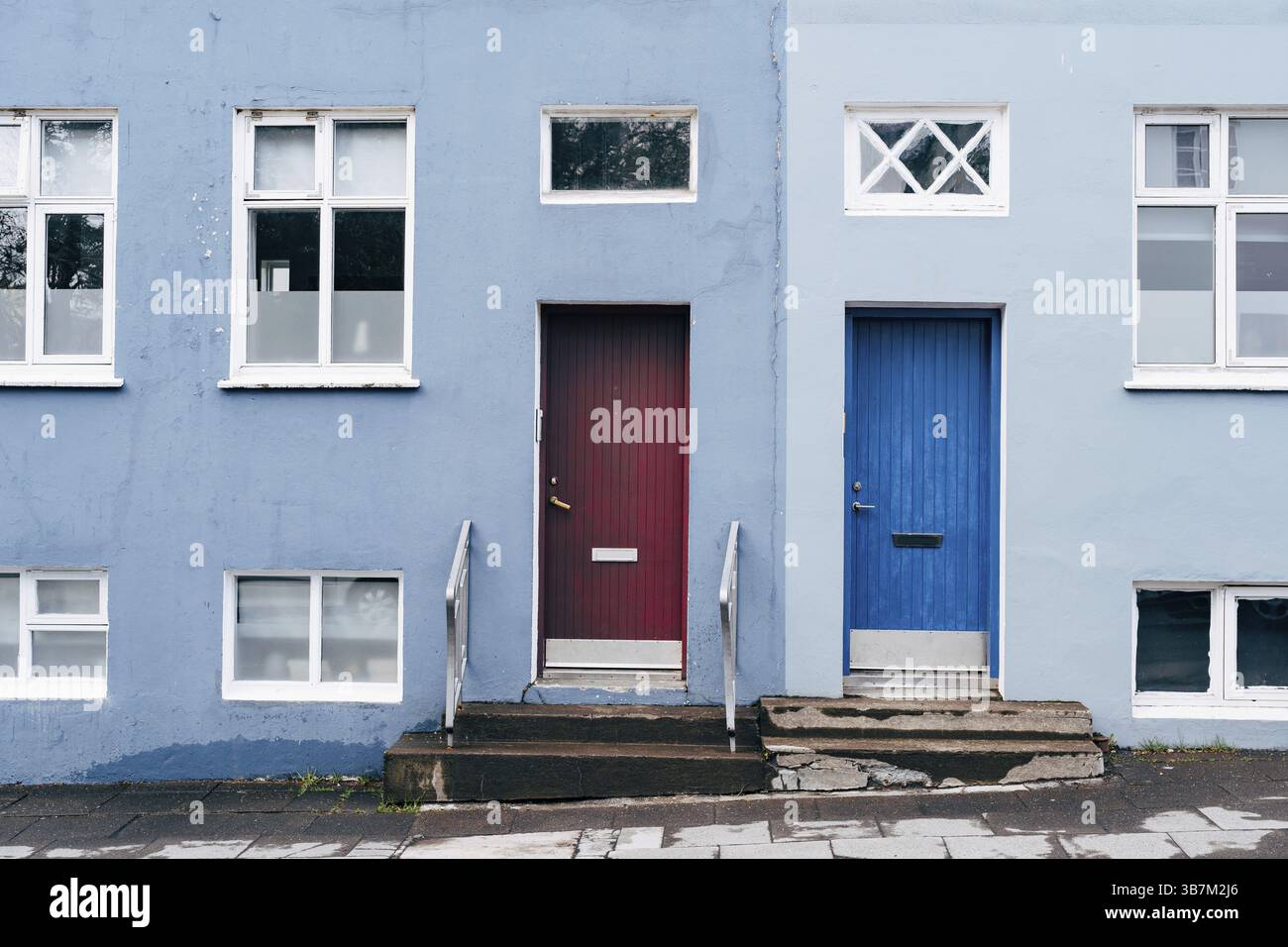 Ein zweifarbiges Gebäude in Blau und Hellblau mit zwei rechteckigen Türen in Blau und Burgund und Fenstern in verschiedenen Größen. Stockfoto
