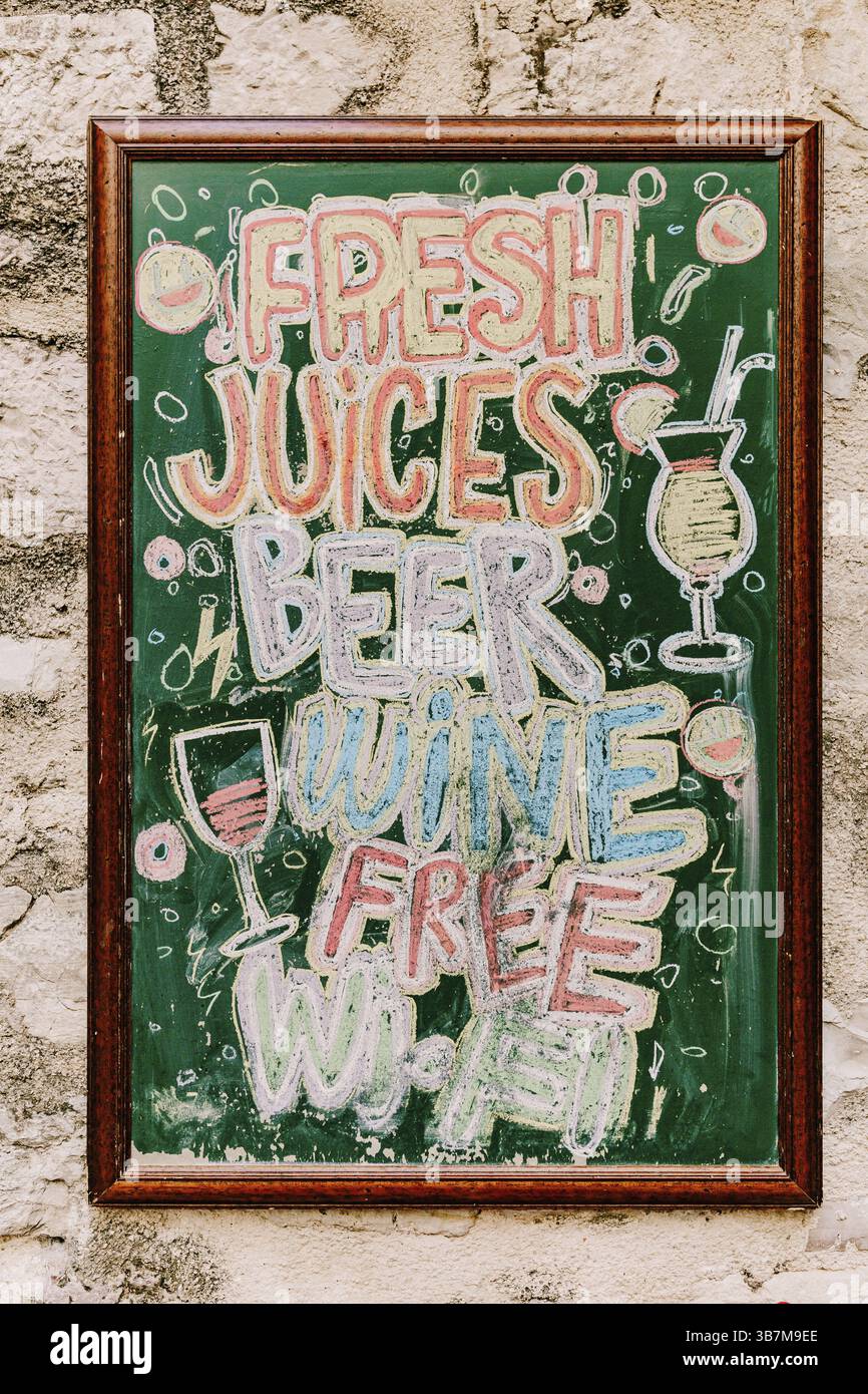 An der Steinwand des Gebäudes hängt eine mit bunten Buntstiften gezeichnete HolzStaffelei. Titel: Frische Säfte Bier Wein kostenloses wi-Fi Stockfoto