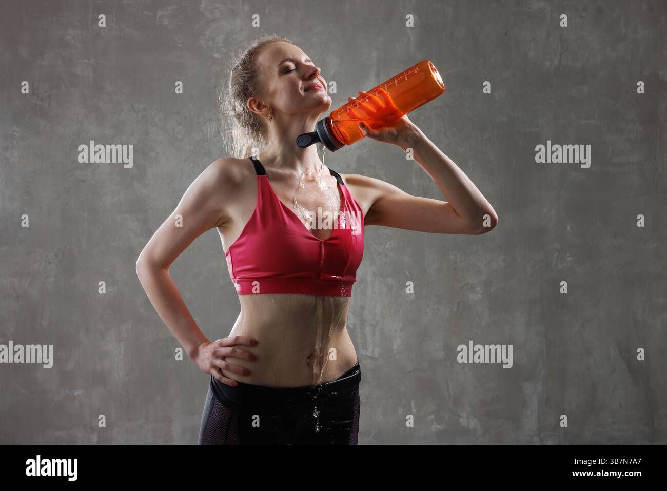 Glückliche junge Frau kühlt sich nach intensivem Training ab, gießt Wasser aus der Flasche auf den Hals und fühlt sich erfrischt. Stockfoto