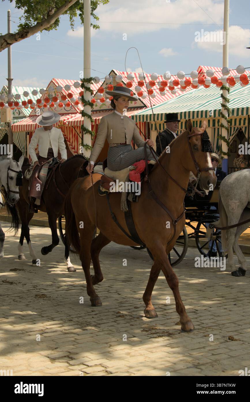Andalusierin auf einem Pferdezug in La Feria de Sevilla 2025, umgeben von farbenfrohen Kasetten und Laternen. Feria de Sevilla, Spanien Stockfoto