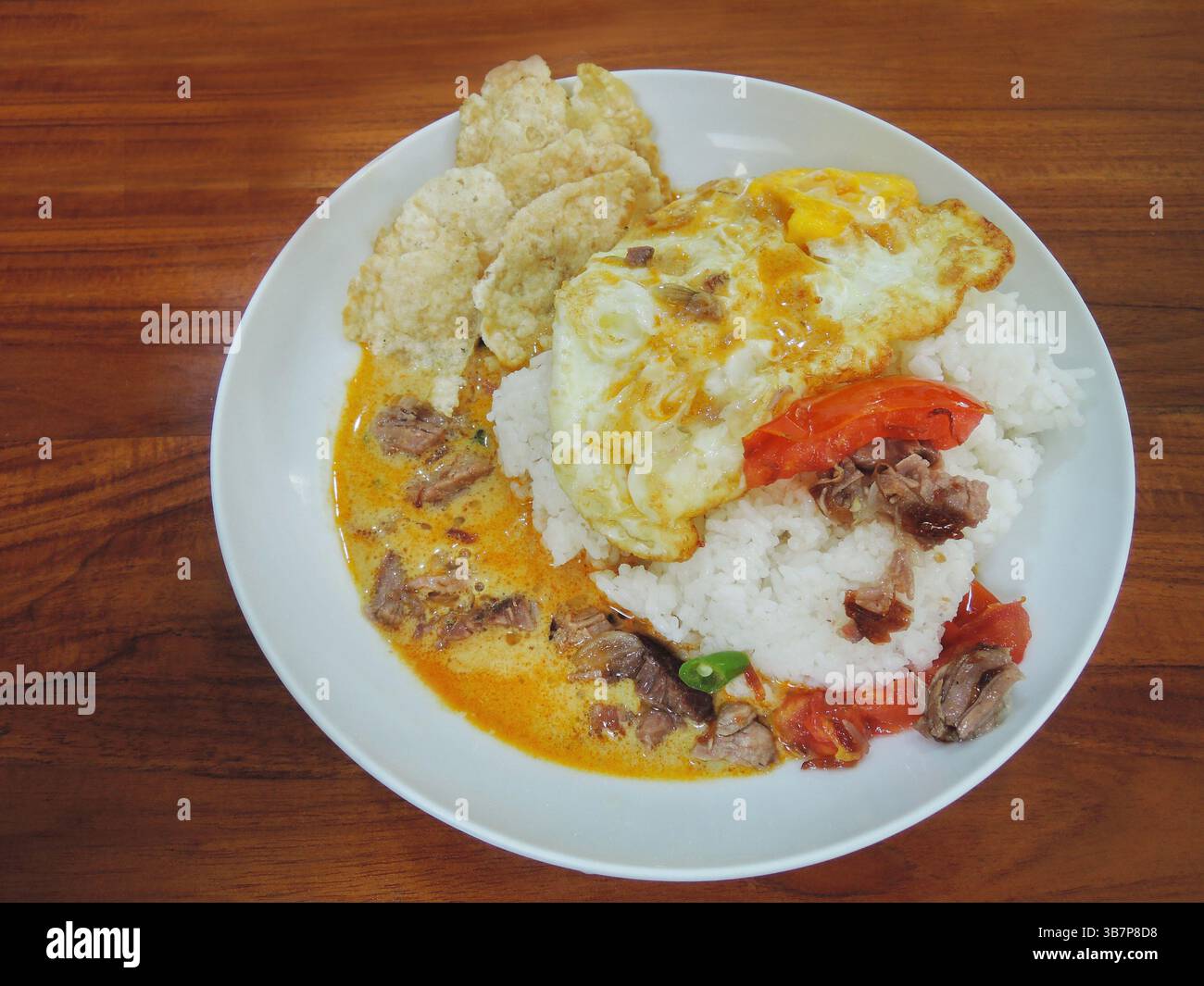 Indonesisches Essen: Soto Betawi, eine Suppe auf Kokosnussbasis mit kleinen Rindfleischstücken oder Schlachtnebenerzeugnissen, serviert mit Reis und leeren Crackern. Stockfoto