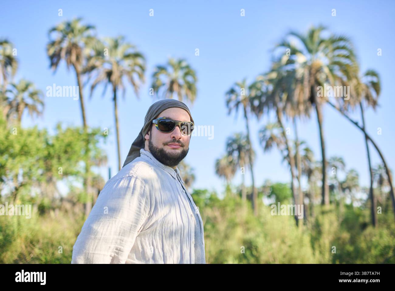 Porträt eines jungen Mannes mit Sonnenbrille, der an einem sonnigen Tag draußen geht, mit Palmen im Hintergrund. Reisende genießen die Natur in El Palmar Nati Stockfoto