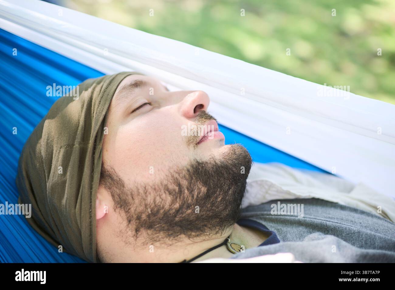 Porträt eines jungen Mannes, der friedlich in einer Hängematte schläft, draußen an einem sonnigen Tag. Sein Ausdruck vermittelt Ruhe und Wohlbefinden. Stockfoto