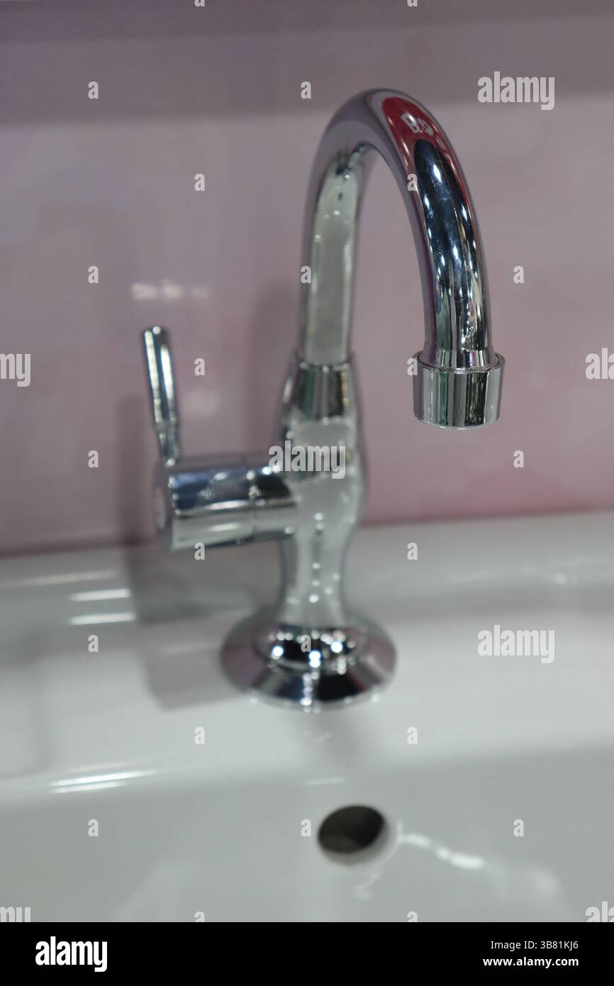 Clean Close Up erfasst einen modernen, polierten Chrom-Wasserhahn, der über einem makellos weißen Keramikwaschbecken montiert ist und die Armaturen des Badezimmers und die schlichte Eleganz hervorhebt Stockfoto