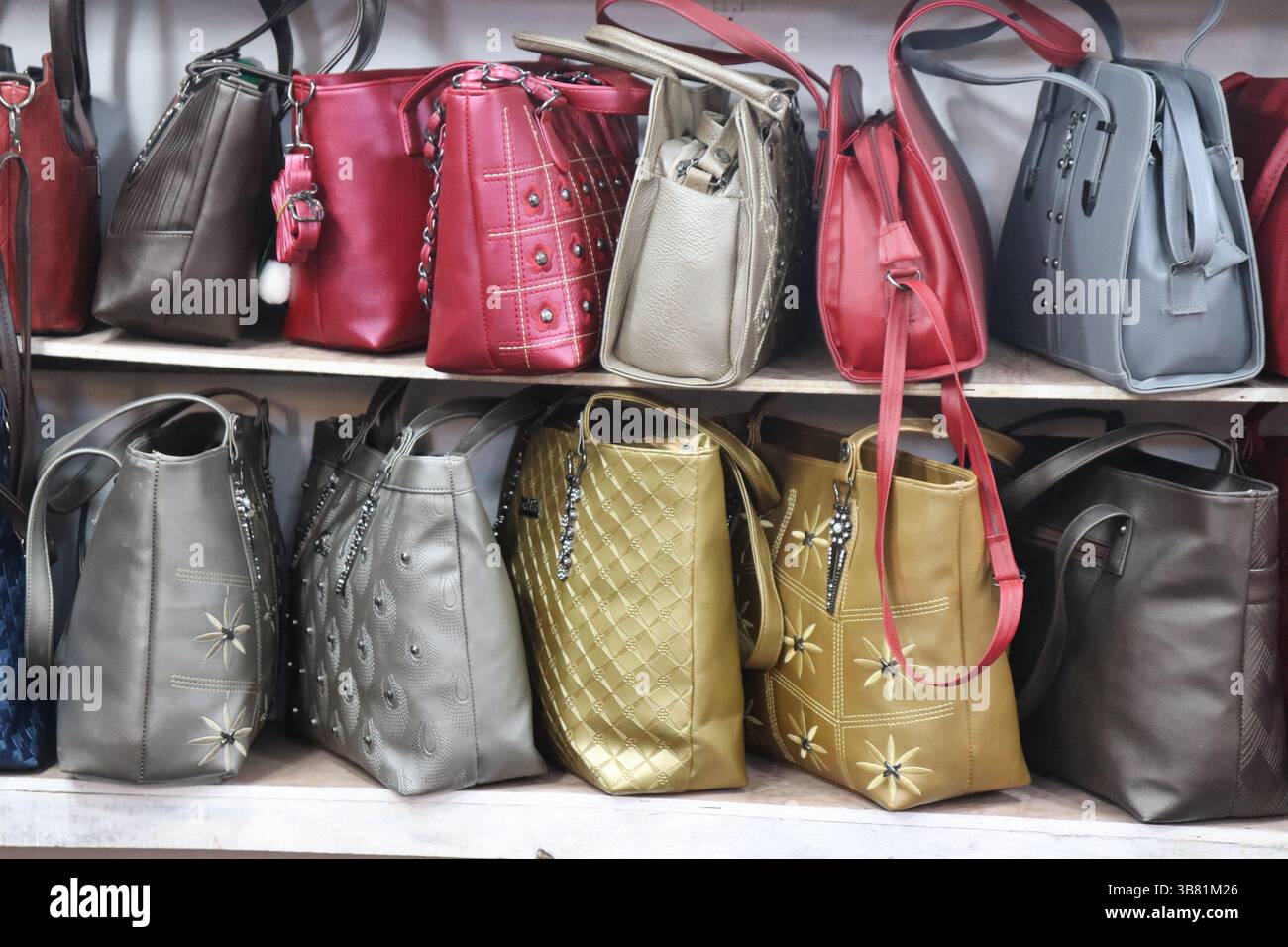 Eine vielfältige Kollektion von Ledertaschen in auffälligen Farben wie Rot, Gold, Grau und Braun ist in Regalen ordentlich angeordnet und zeigt unterschiedliche Formen Stockfoto