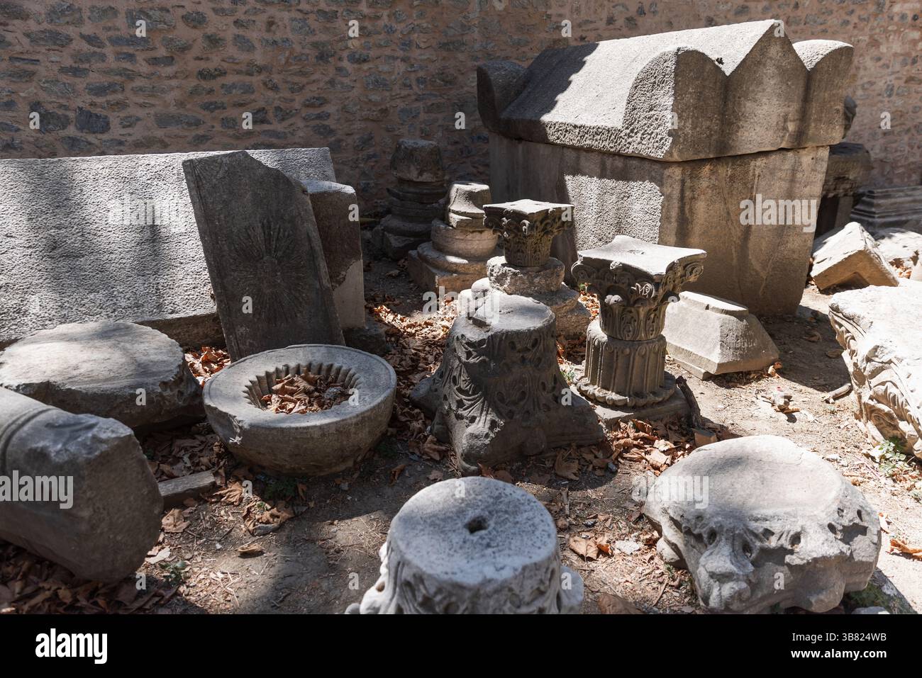 Antike Steinartefakte, darunter ein Sarkophag und architektonische Fragmente, verstreut in einem offenen Bereich, umgeben von einer Steinmauer. Antiquitäten werden hervorgehoben Stockfoto Antike Steinartefakte, darunter ein Sarkophag und architektonische Fragmente, verstreut in einem offenen Bereich, umgeben von einer Steinmauer. Antiquitäten werden hervorgehoben Stockfoto
