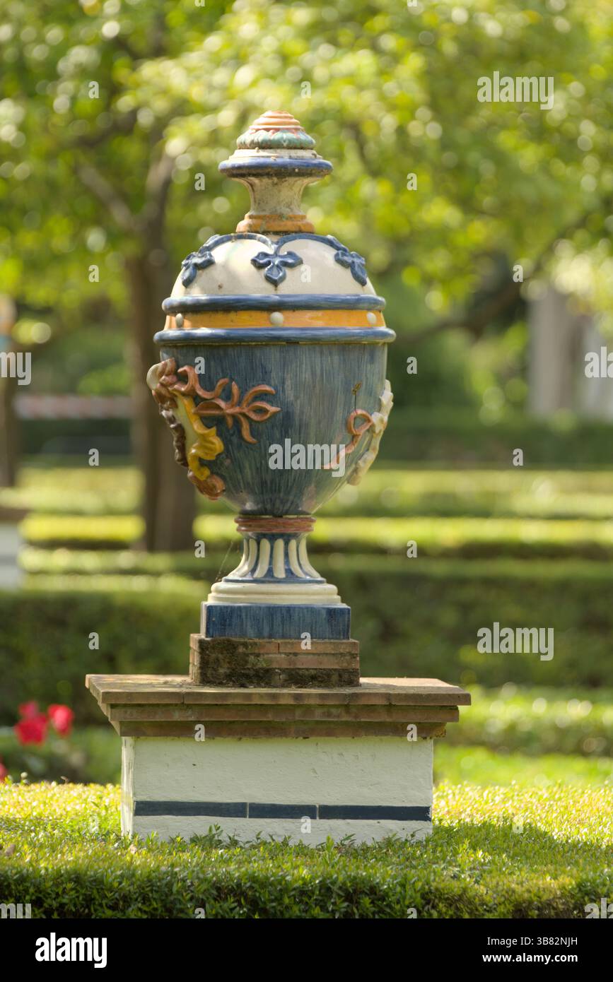 Dekorative Keramikurne auf einem Steinsockel in einem sonnendurchfluteten andalusischen Garten mit traditioneller spanischer Handwerkskunst. Sevilla, Spanien Stockfoto