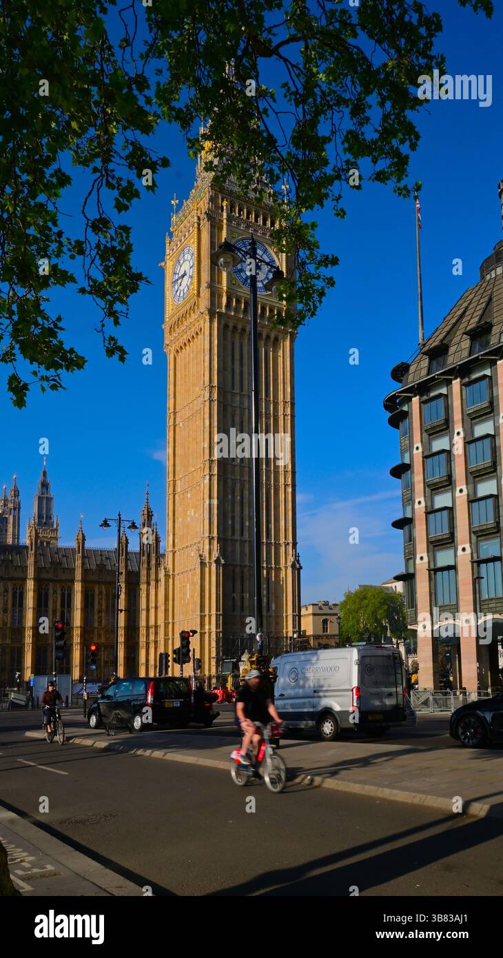 Big Ben im Morgenlicht von Victoria Embankment mit Blick nach Süden mit Radfahrern und Fahrzeugen und überhängendem Baum im Blatt und blauem Himmel Stockfoto