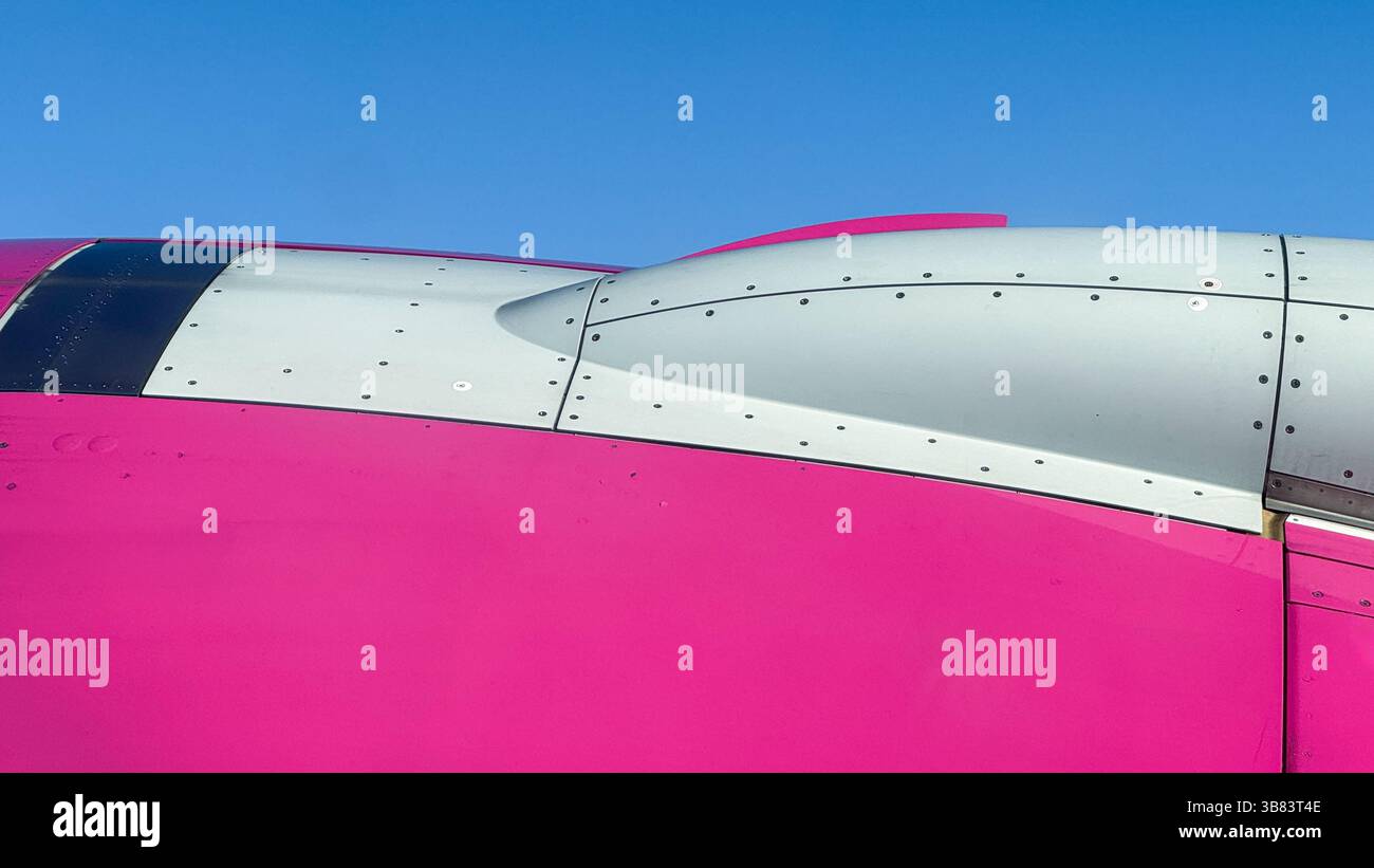 Nahaufnahme des rosafarbenen und weißen Flugzeugrumpfes vor klarem blauem Himmel, was die Ästhetik des modernen Flugzeugdesigns und die technische Präzision unterstreicht. Stockfoto