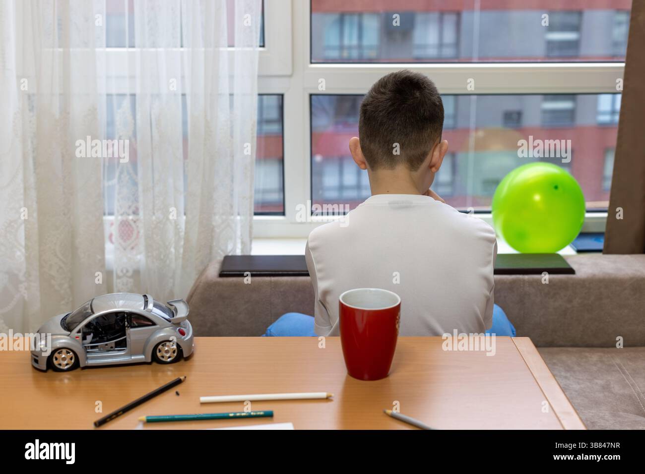 Rückansicht eines Jungen, der am Fenster sitzt und in ruhiger und nachdenklicher Stimmung nach draußen blickt. Stockfoto