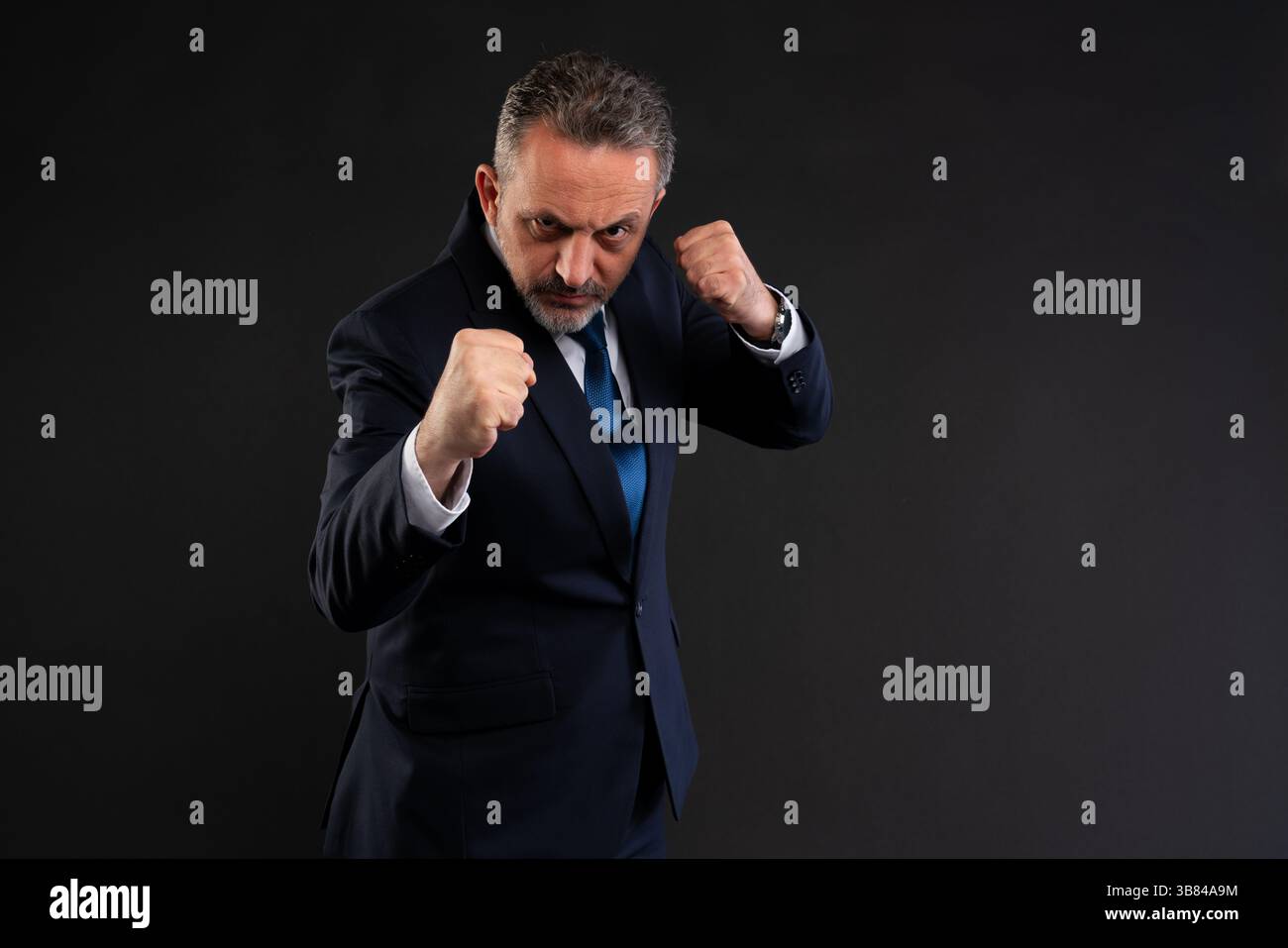 Seriöser Geschäftsmann im Anzug mit geballten Fäusten vor ihm, bereit zum Kampf. Symbol für Entschlossenheit, Resilienz und unternehmerische Kampfbereitschaft. Bolzen Stockfoto