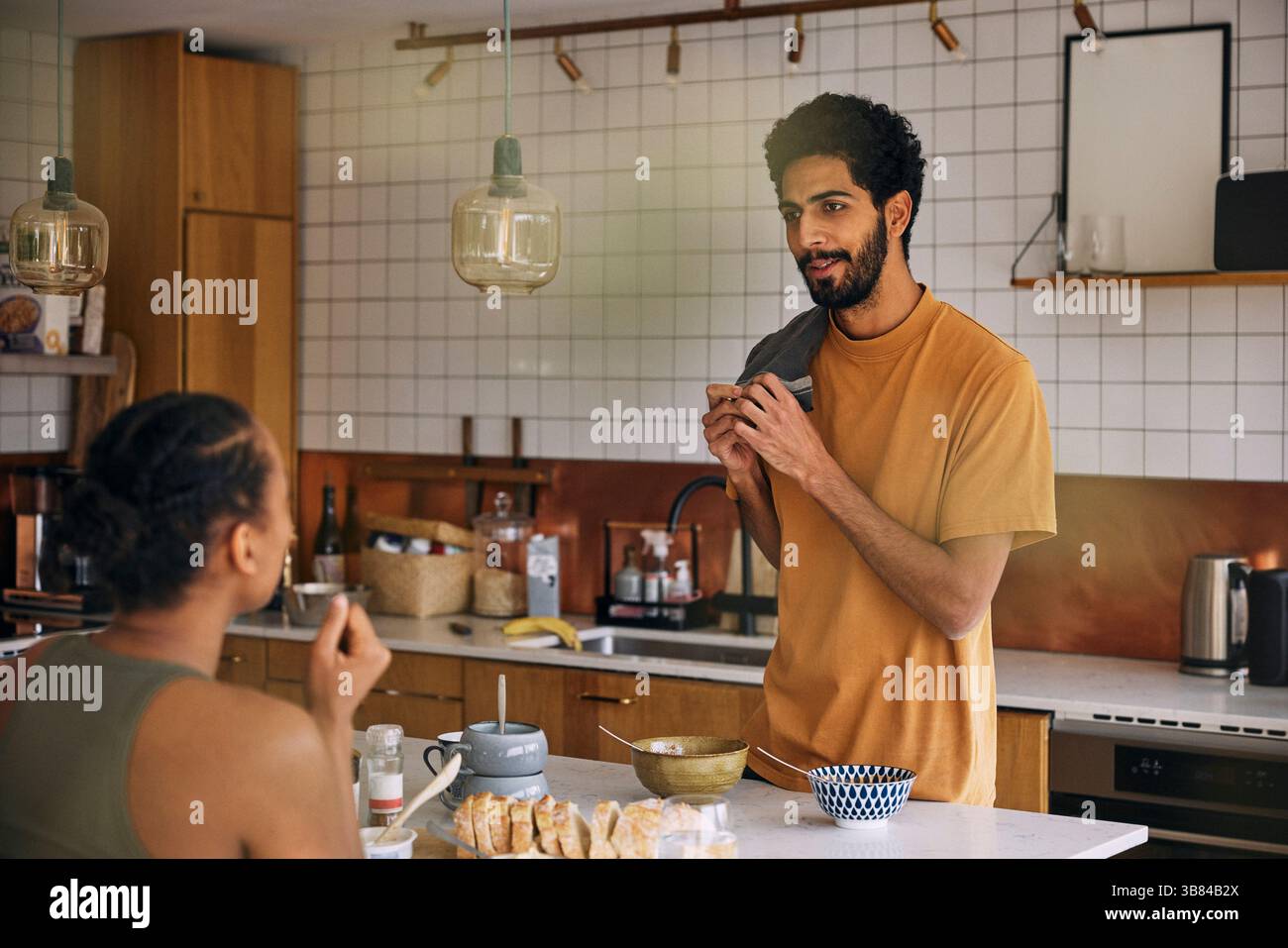 Mann, der in der Nähe der Kücheninsel steht, während er mit der Freundin beim Frühstück zu Hause sprach Stockfoto