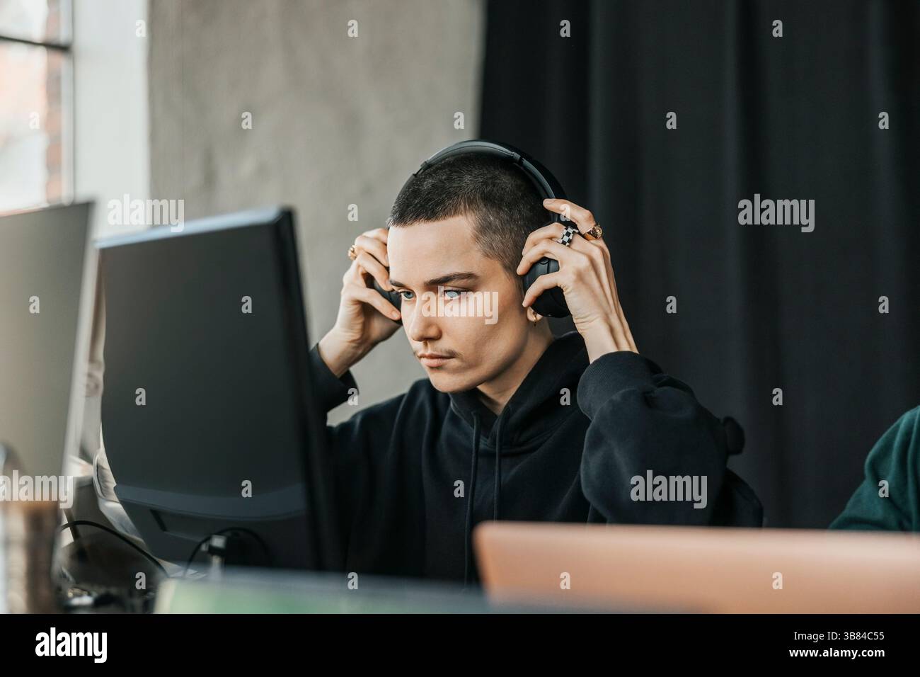 Nicht binärer Unternehmer, der schnurlose Kopfhörer trägt, während er im Büro am Desktop-PC arbeitet Stockfoto