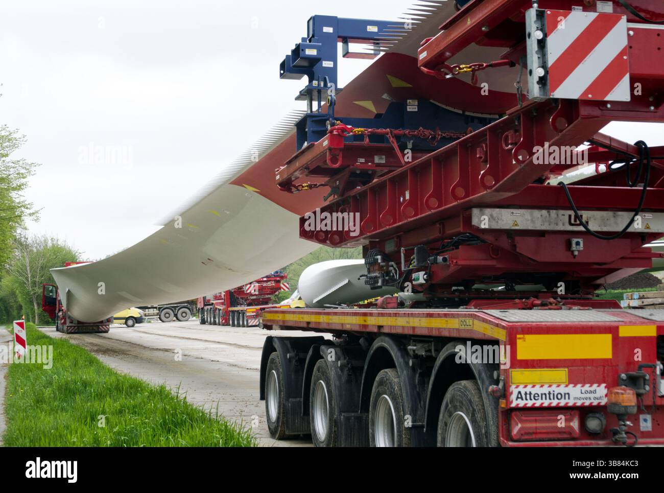 Spezialisierte Lkw transportieren ein sehr langes Windenergieblatt entlang einer Landstraße und zeigen die Logistik der Infrastruktur für erneuerbare Energien Stockfoto