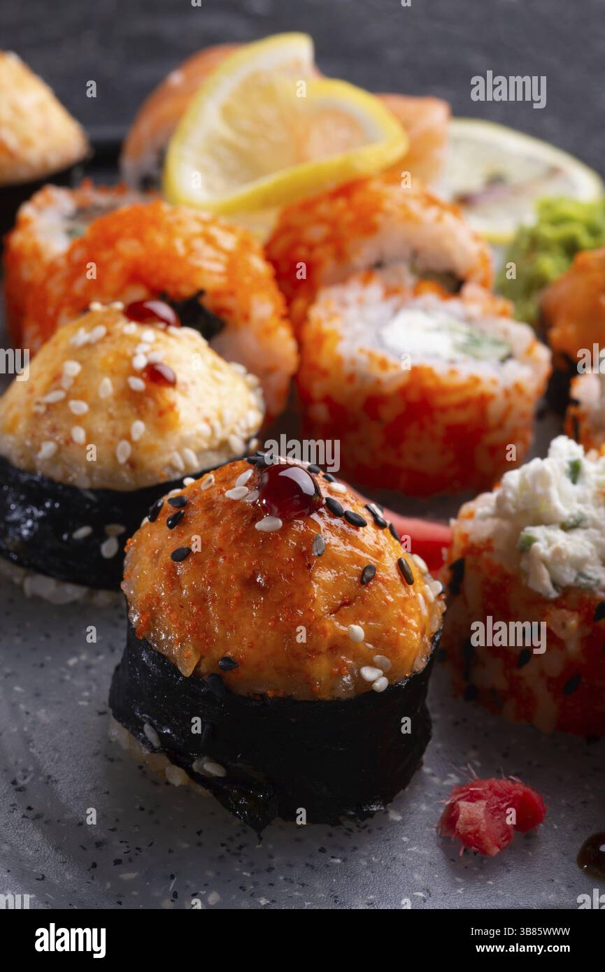 Sushi-Rollenset serviert auf grauem Tablett am schwarzen Tisch. Flach verlegt. Schließen Stockfoto