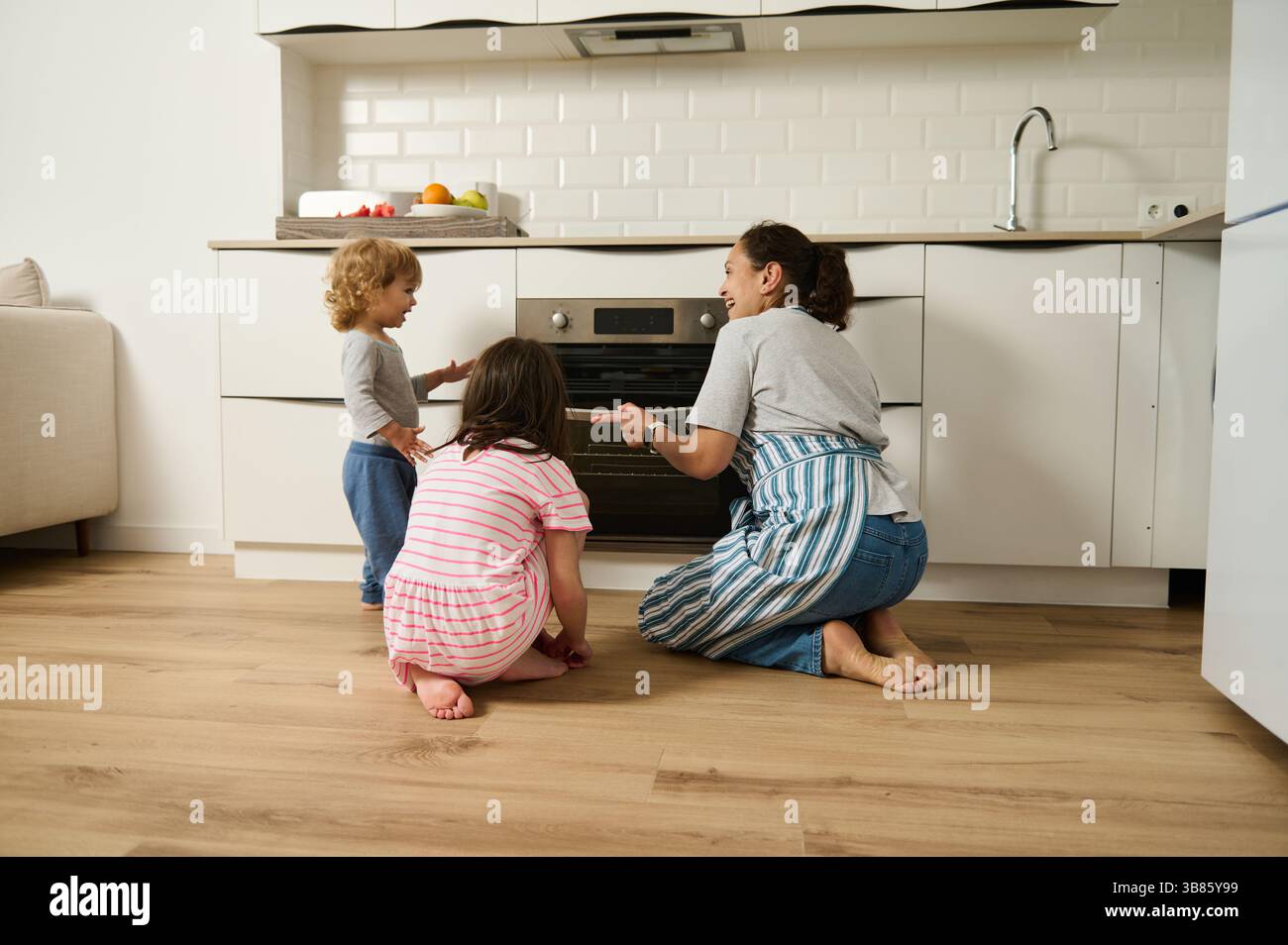 Eine Mutter und ihre beiden Kinder backen fröhlich zusammen in einer modernen Küche. Die Familie bereitet gerne hausgemachte Gerichte zu und fördert die Kreativität Stockfoto
