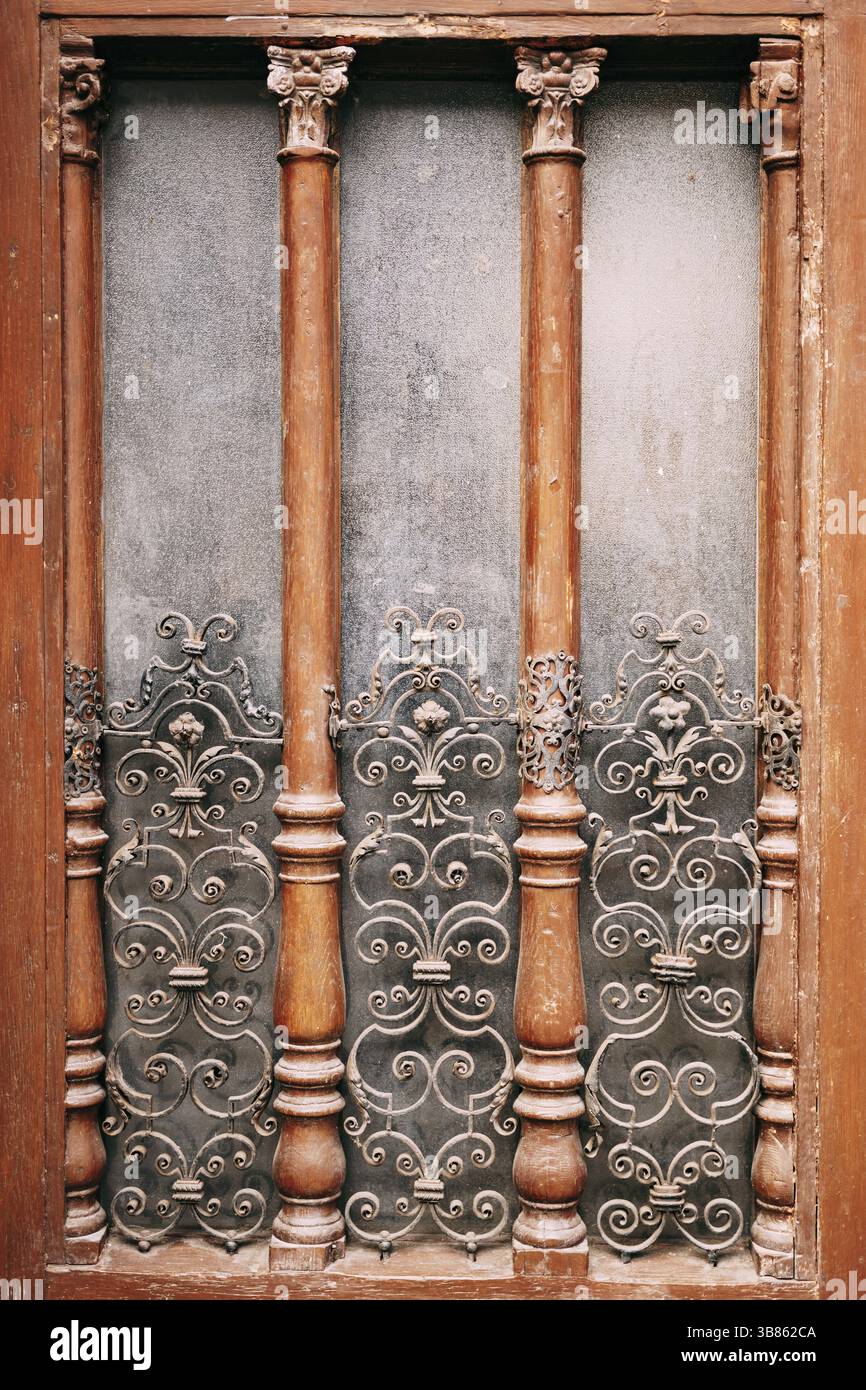 Ein Holzfenster mit einem Metallgitter mit Mustern bis zur Mitte und Holzsäulen. Stockfoto
