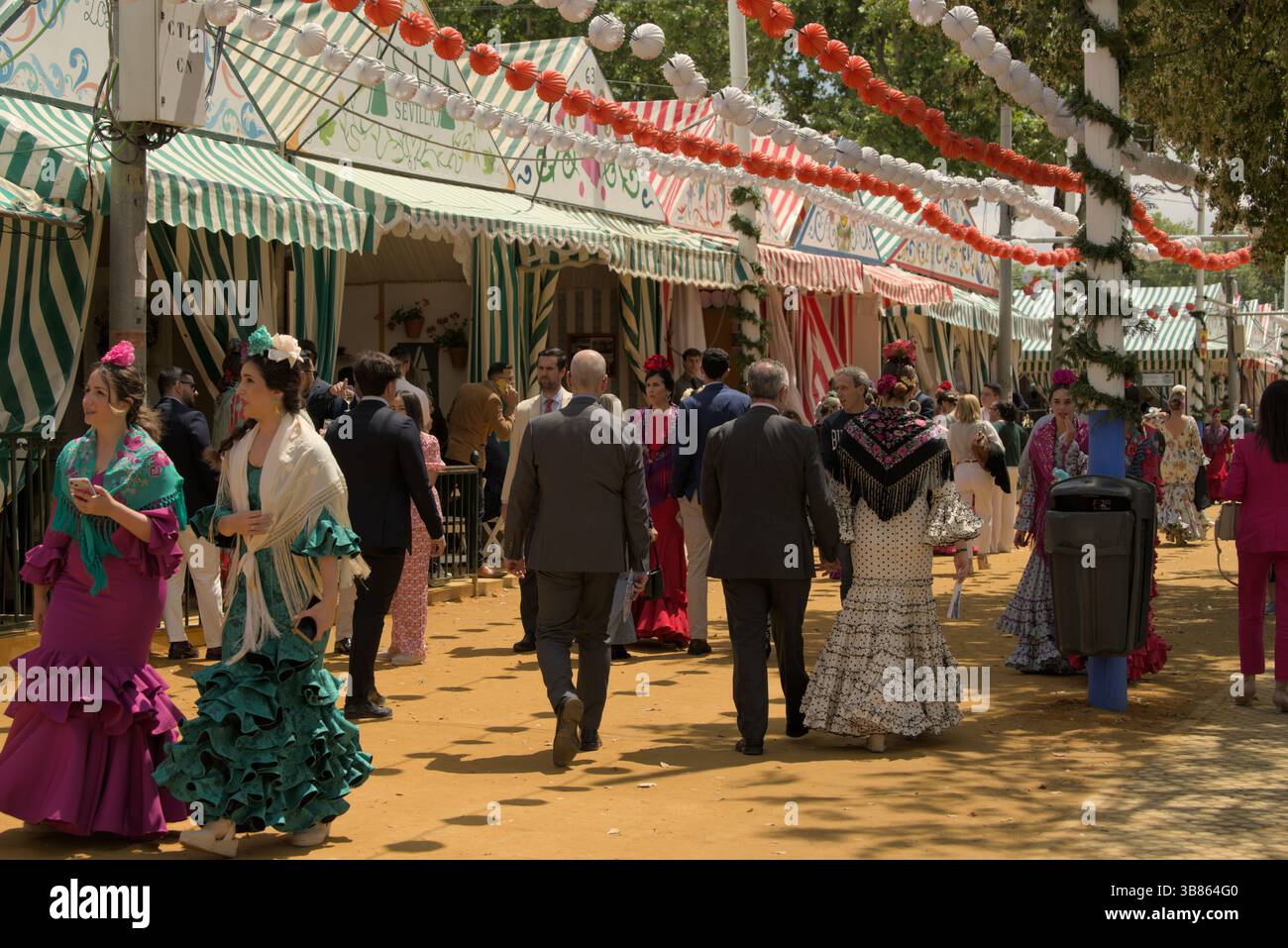 Menschen in traditioneller andalusischer Kleidung feiern die Feria de Abril in Sevilla, Spanien, umgeben von farbenfrohen Zelten und festlichen Dekorationen. Stockfoto