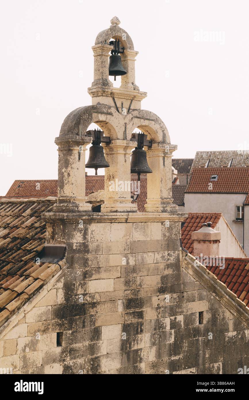 Drei Glocken auf einem alten Steinglockenturm vor einem Hintergrund von gekachelten Dächern. Stockfoto