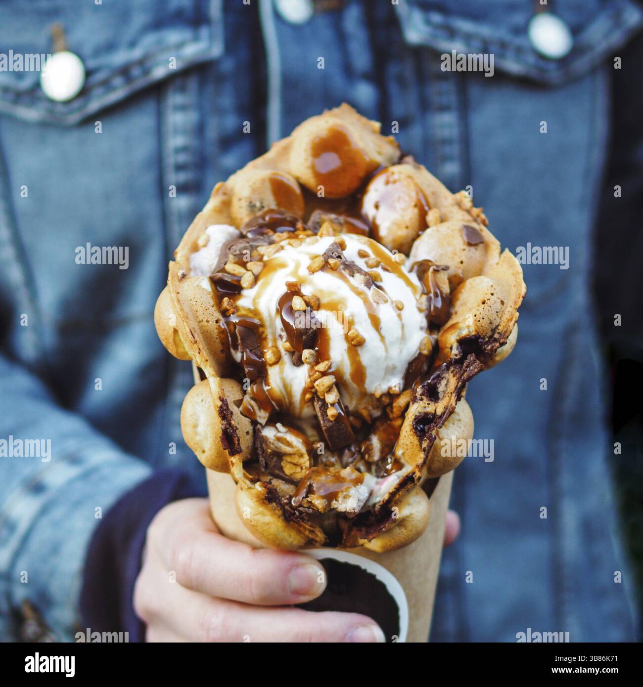 Hong Kong Waffeln in weiblicher Hand. Mädchen in Jeans Jacke halten Sie köstliche bubble Waffeln mit Eis und Karamell Sirup. Trendy essen. Platz Stockfoto