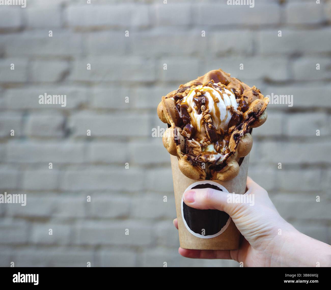 Hong Kong Waffeln in weiblicher Hand auf Mauer Hintergrund. Köstliche bubble Waffeln mit Eis und Karamell Sirup in der Frau die Hand. Trendy essen. Kopieren s Stockfoto