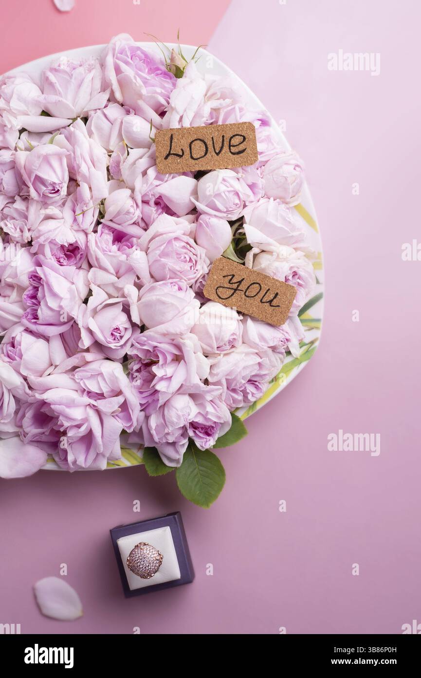 Teller mit rosafarbenen Rosen mit Ring um rosa Hintergrund. Romantisches und Schönheitskonzept Stockfoto