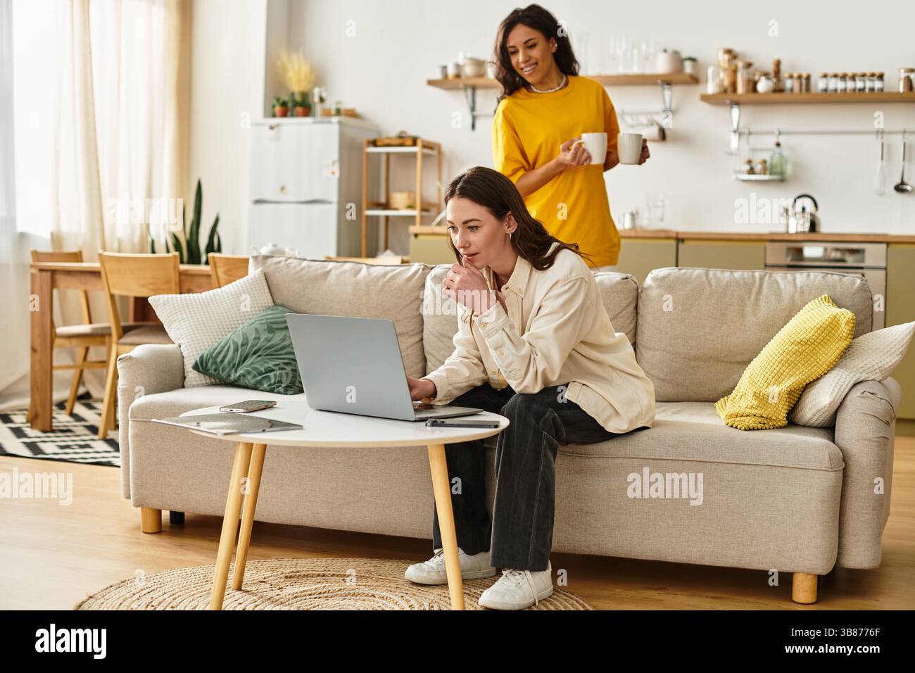 Zwei Frauen verbringen einen warmen Moment in ihrem schönen Zuhause, während eine einen Drink genießt und die andere lächelt. Stockfoto