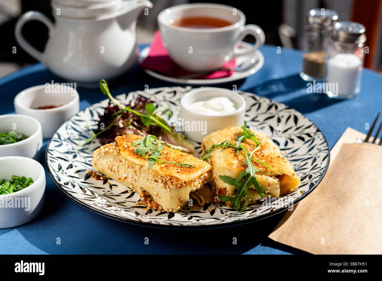 Gebratene Sesamkroketten auf Pfannkuchenteig mit griechischem Jogurt. Serviert auf einem weißen Teller. Ein frisches und leckeres Frühstücksset, beleuchtet von der Morgensonne. Stockfoto