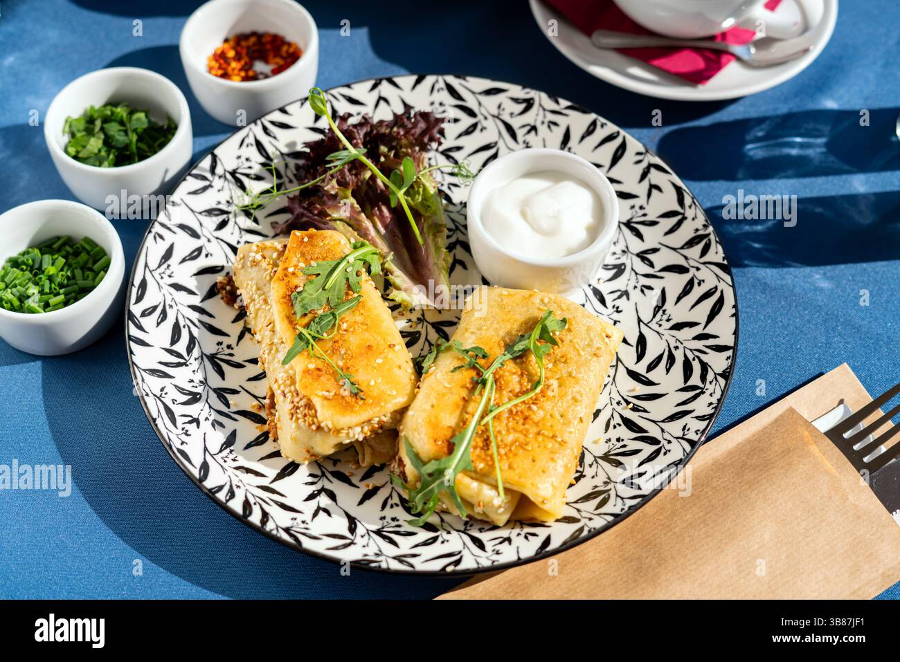 Gebratene Sesamkroketten auf Pfannkuchenteig mit griechischem Jogurt. Serviert auf einem weißen Teller. Ein frisches und leckeres Frühstücksset, beleuchtet von der Morgensonne. Stockfoto