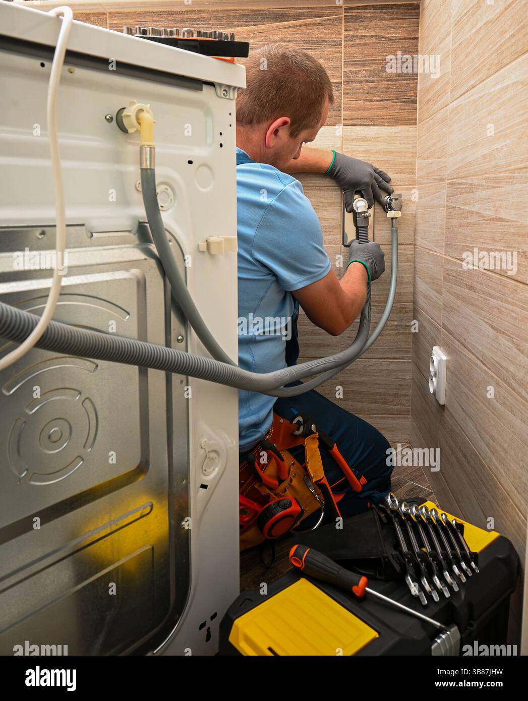 Professioneller Klempner, der den Wasserversorgungsschlauch an die Waschmaschine im Badezimmer anschließt, gewährleistet eine ordnungsgemäße Installation und Funktionalität. Stockfoto