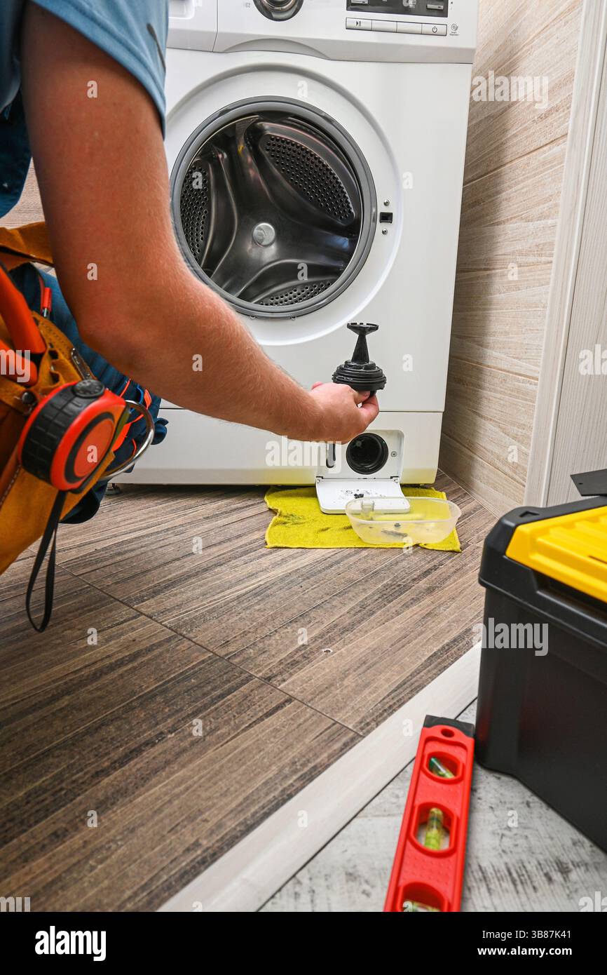 Klempner hält eine Waschmaschinenpumpe während der Wartungsarbeiten im Badezimmer. Stockfoto