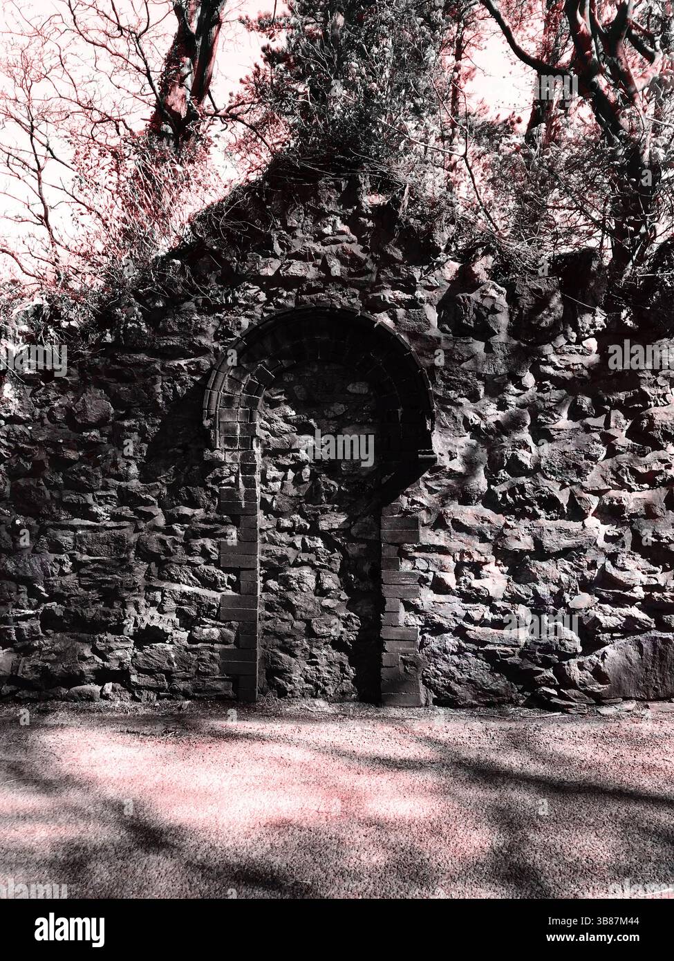 Gemauertes Tor, Bäume dahinter, Schatten in rot, die auf etwas verstecktes, verlassenes, vergessenes Fantasy-Märchenreich hinweisen Stockfoto