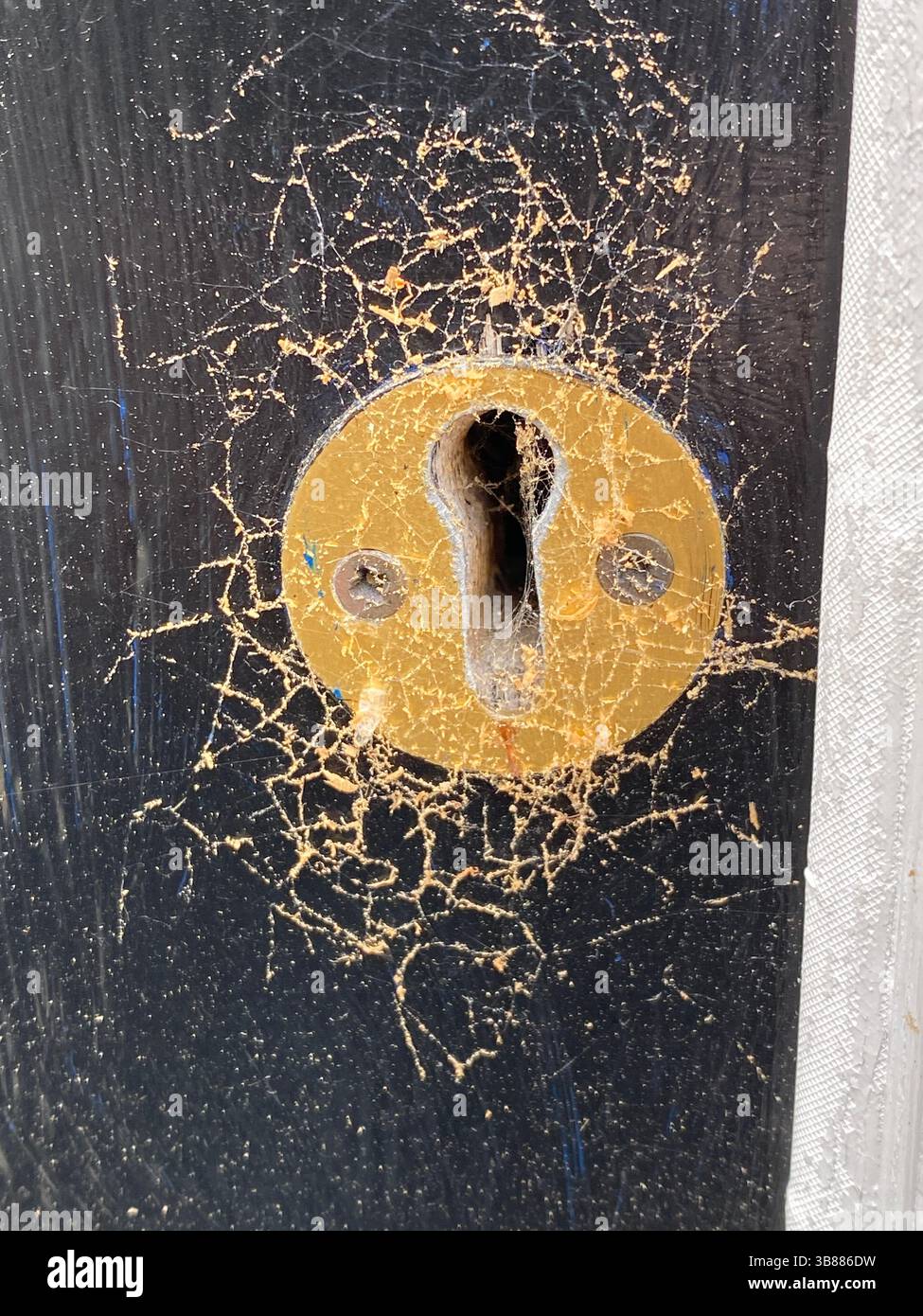 Nahaufnahme eines staubigen Schlüssellochs aus Messing, das mit Spinnweben bedeckt ist, an einer verwitterten schwarzen Tür, das Zeichen von Alter und Vernachlässigung zeigt. - Smartphone-aufgenommenes Stockfoto