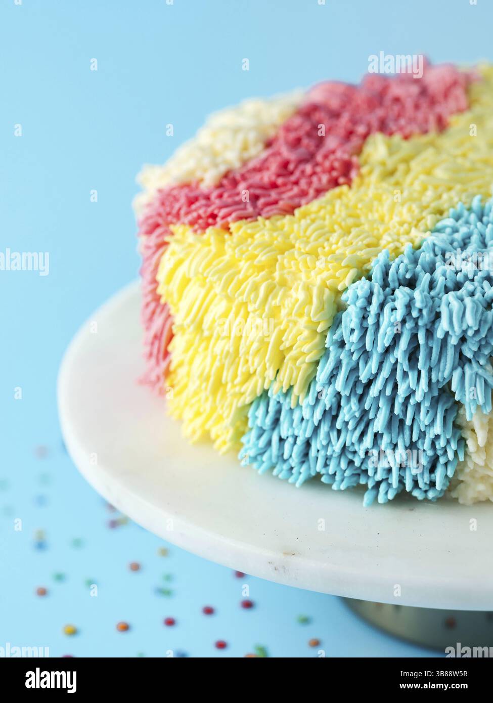 Fick Kuchen auf blauem Hintergrund. Lustiger, bunter Vanille-Shag-Kuchen mit perfekter Vanille-Buttercreme. Idee von optisch ansprechenden Kuchendekorationsschemata, tr Stockfoto