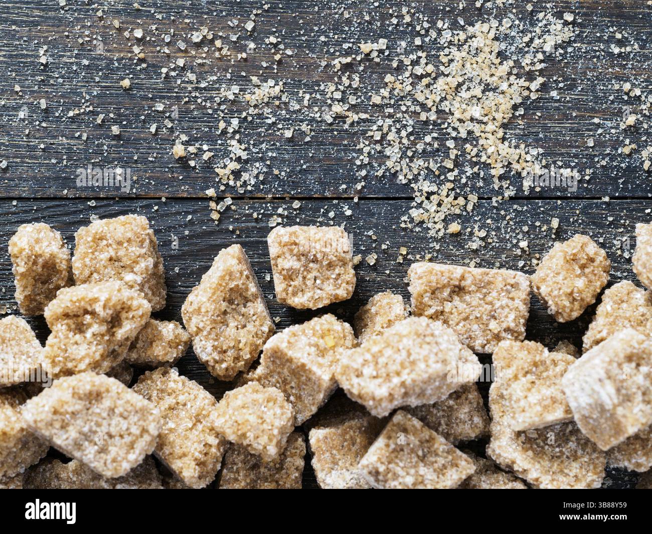 Natürliche rohe braune Rohrzuckerwürfel und brauner Kristallzucker auf braunem hölzernem Hintergrund. Draufsicht auf braunen Zucker mit Copyspace Stockfoto