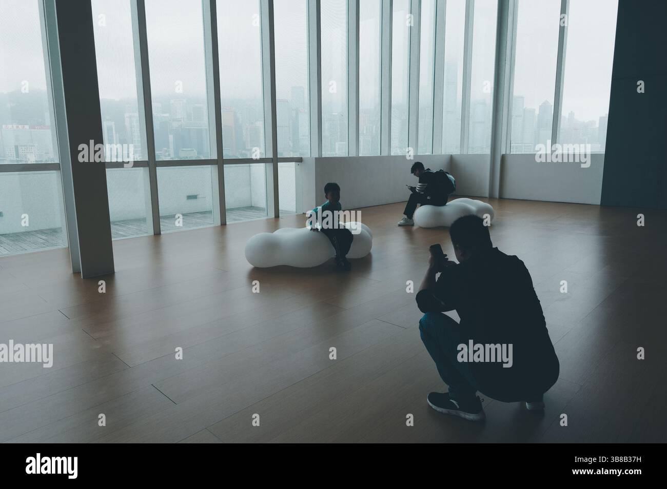 Vater macht eine Aufnahme, um ein Foto seines Kindes zu machen, das vor der Kulisse der Skyline von Hongkong am HKMoA sitzt Stockfoto