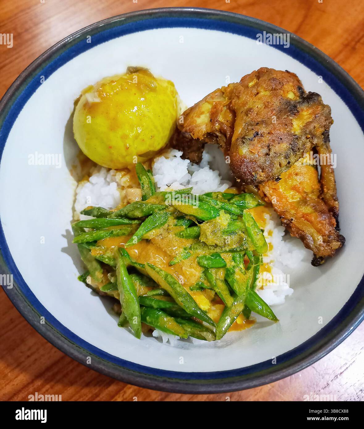 Indonesische Mahlzeit aus Ayam-Bakar oder gegrilltem Huhn, Gulai Telur oder gekochtem Ei in mildem Curry und Buncis oder in Scheiben geschnittenen langen grünen Bohnen. Stockfoto