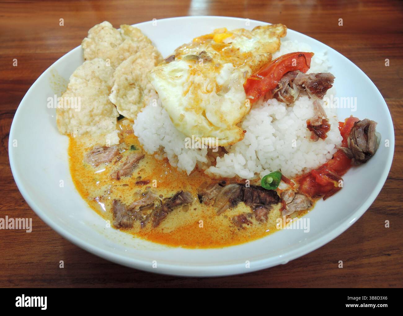 Indonesisches Essen - Soto Betawi, eine Suppe auf Kokosnussbasis mit kleinen Rindfleischstücken oder Schlachtnebenerzeugnissen, serviert mit Reis, Spiegelei und leeren Crackern. Stockfoto