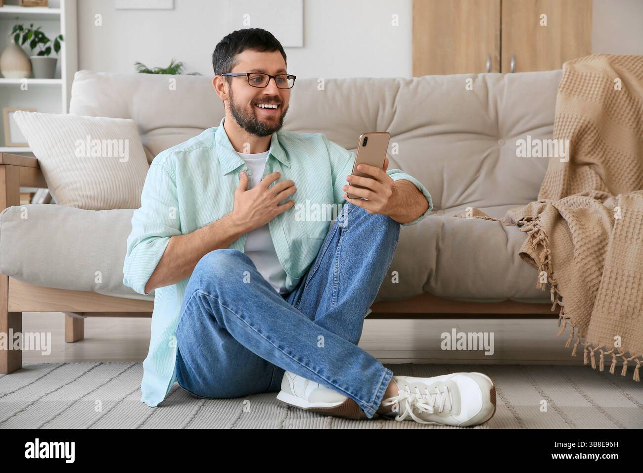 Überraschter junger Mann, der zu Hause ein Handy benutzt Stockfoto